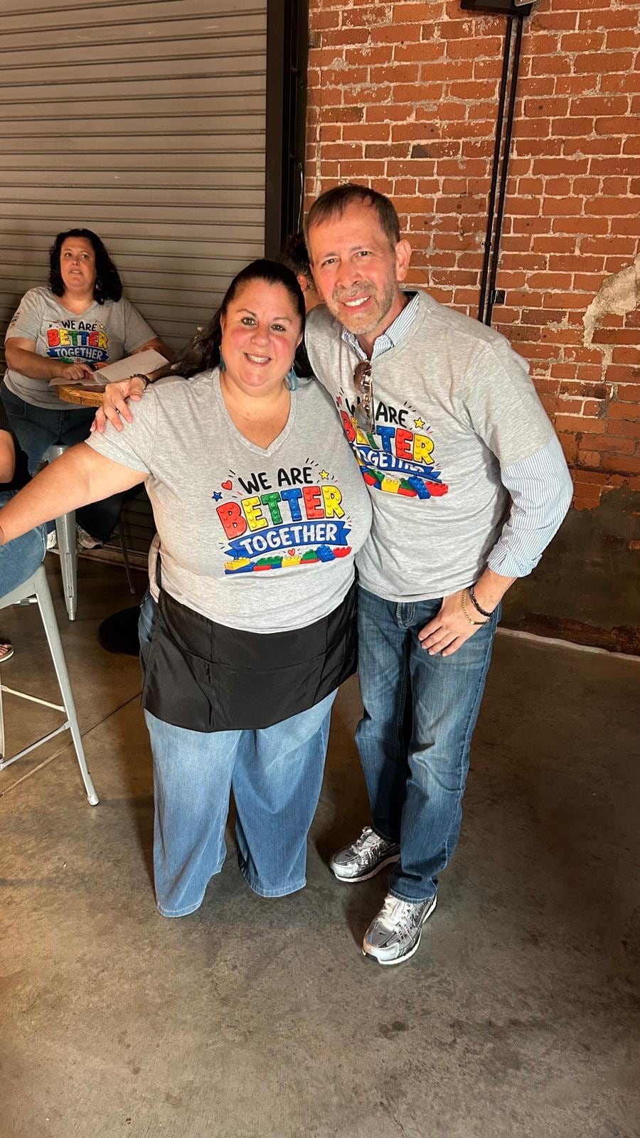 Two women and a man stand close together and smile in front of a brick wall.