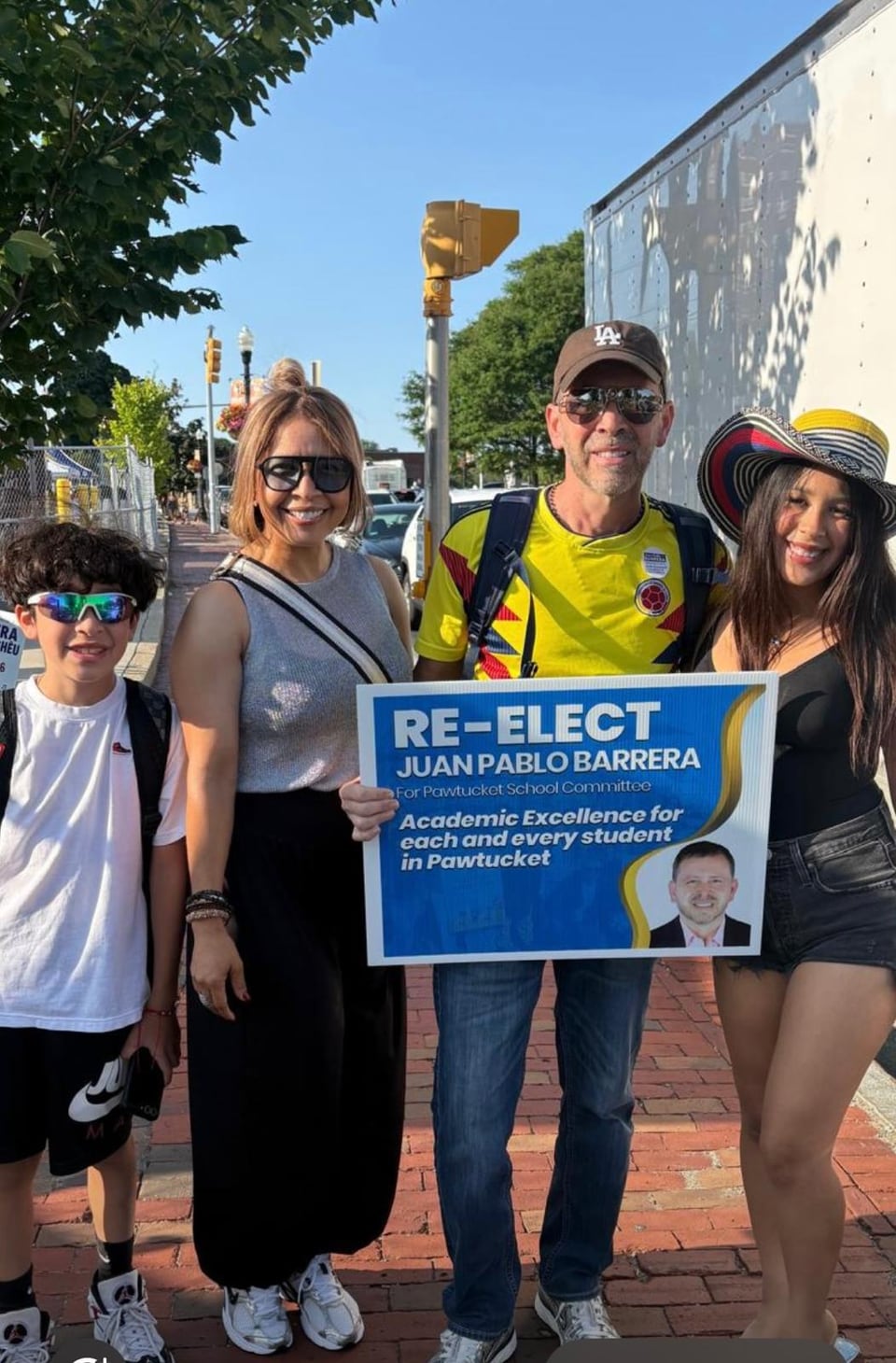 Four people pose outdoors with a blue “Re-elect Juan Pablo Barrera” sign held at center.