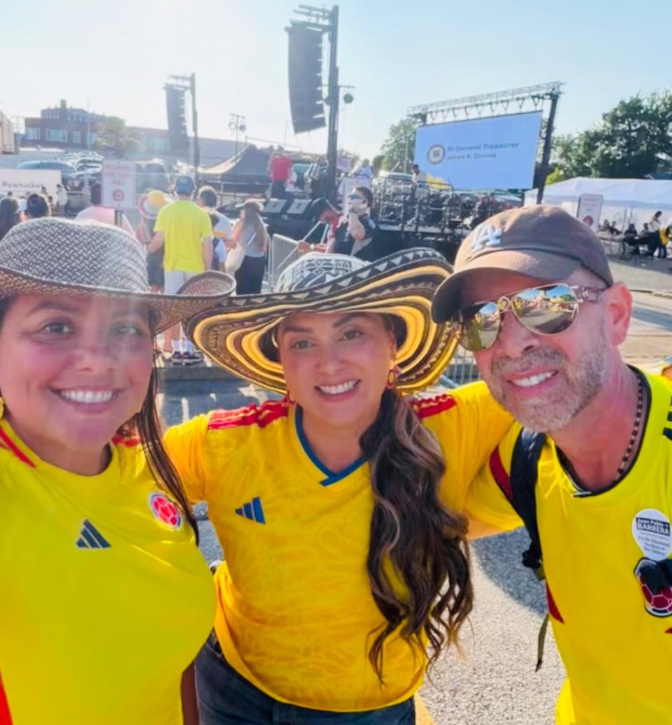 Three people in bright yellow and blue sports jerseys smile for a selfie amid an outdoor crowd.
