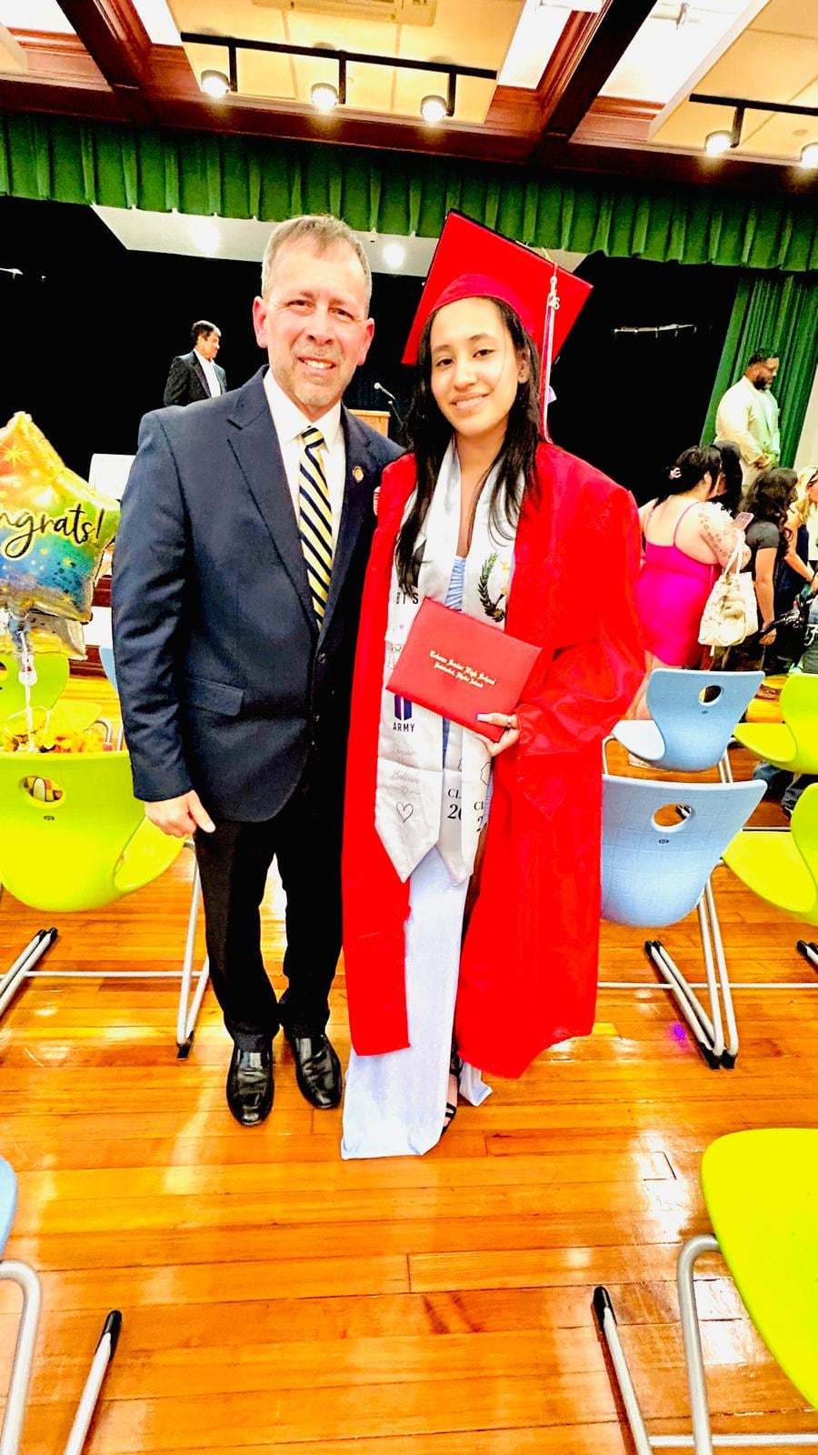 A man in a dark suit and a woman in a white and red outfit pose together in a decorated indoor space.