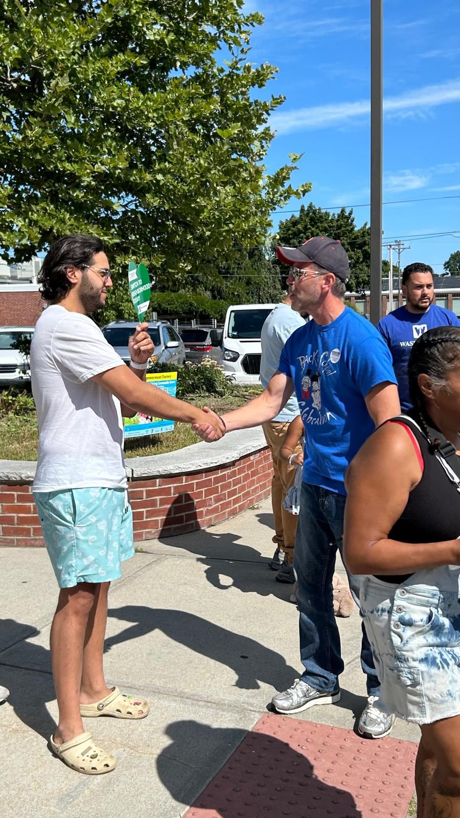A man in a blue shirt shakes hands with a woman in a turquoise top outdoors.