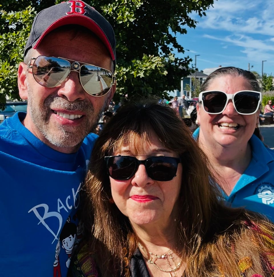 A man in a red cap and two women wearing sunglasses smile for a close-up outdoor selfie.