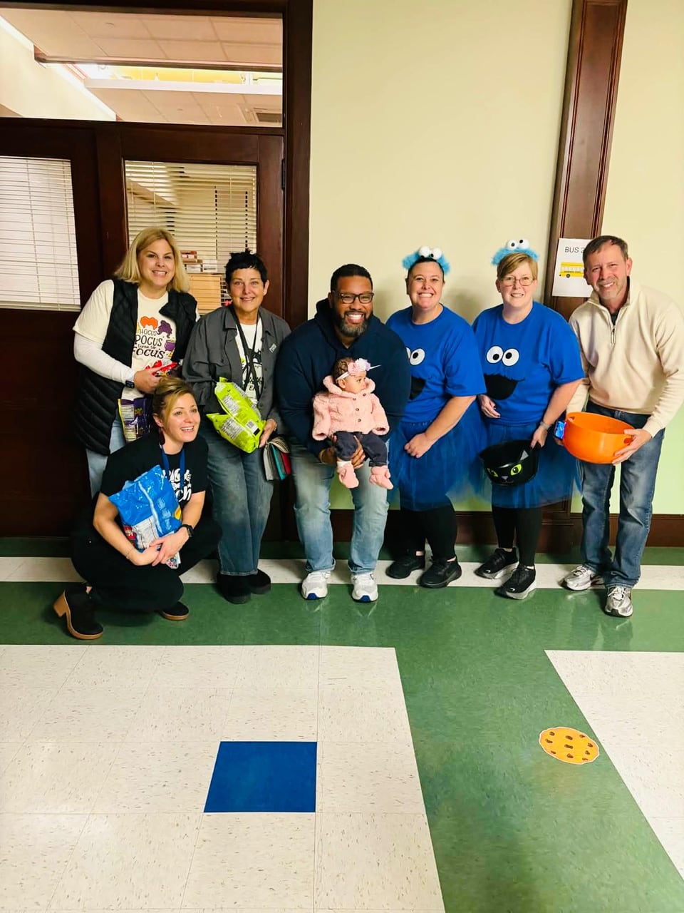 Adults and children pose together in a hallway with a tiled floor.