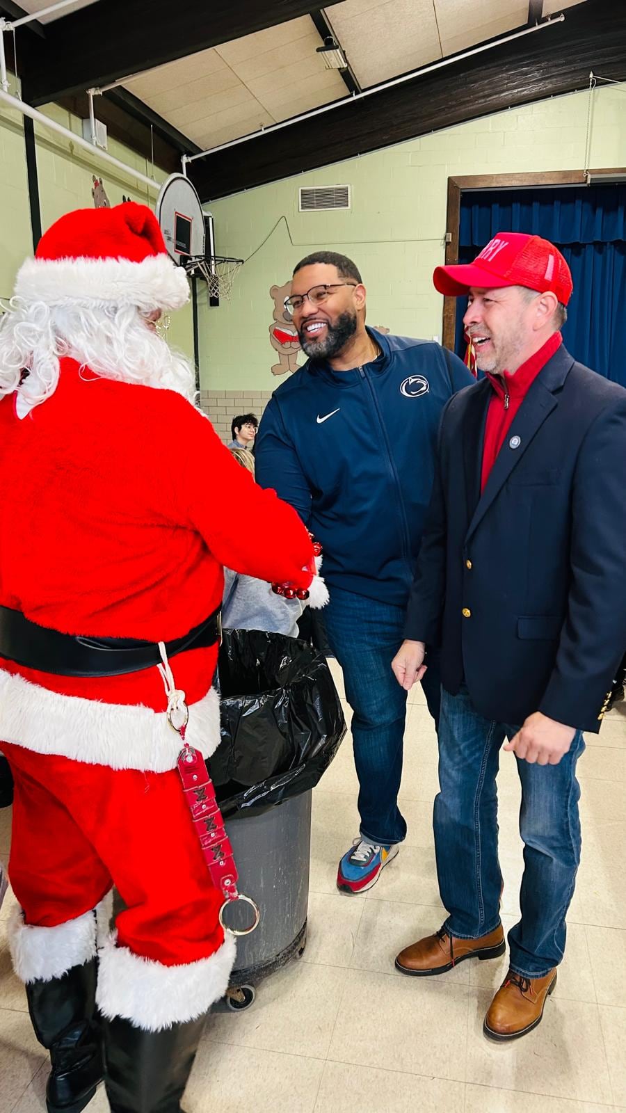 A person dressed as Santa shakes hands with a man in a blue shirt while another man looks on.