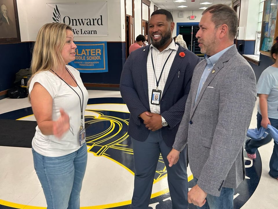 A woman speaks with two men in business attire beside an indoor display.