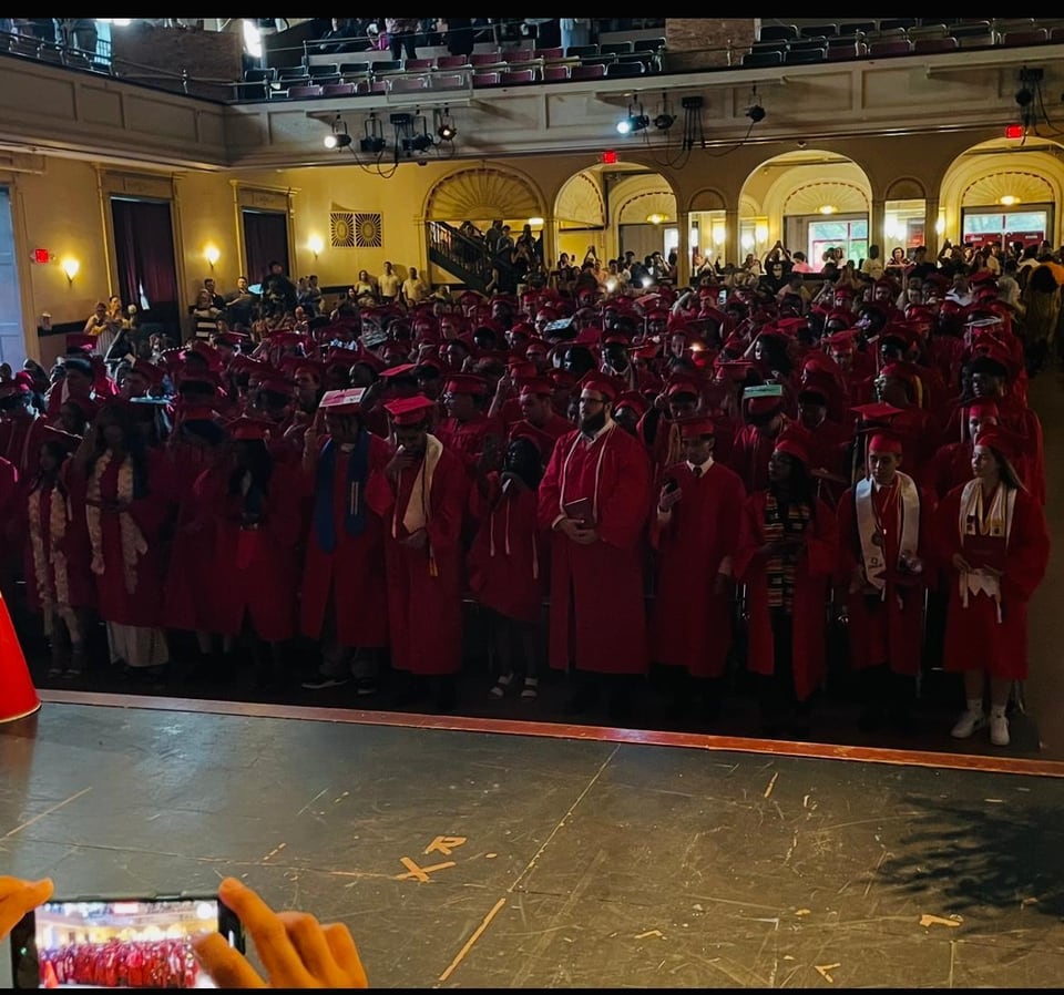 A large crowd dressed mostly in red fills an auditorium as seen from the stage.
