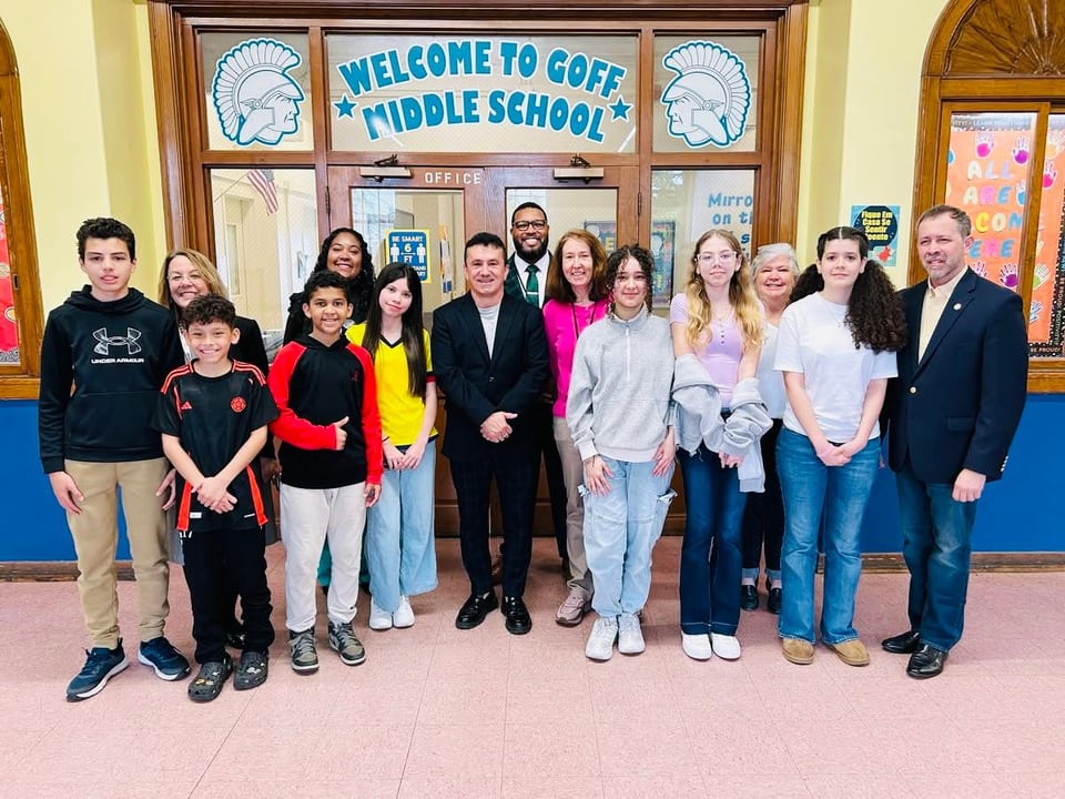 Adults and children pose beneath a 'Welcome to Goff Middle School' sign in an entrance hall.