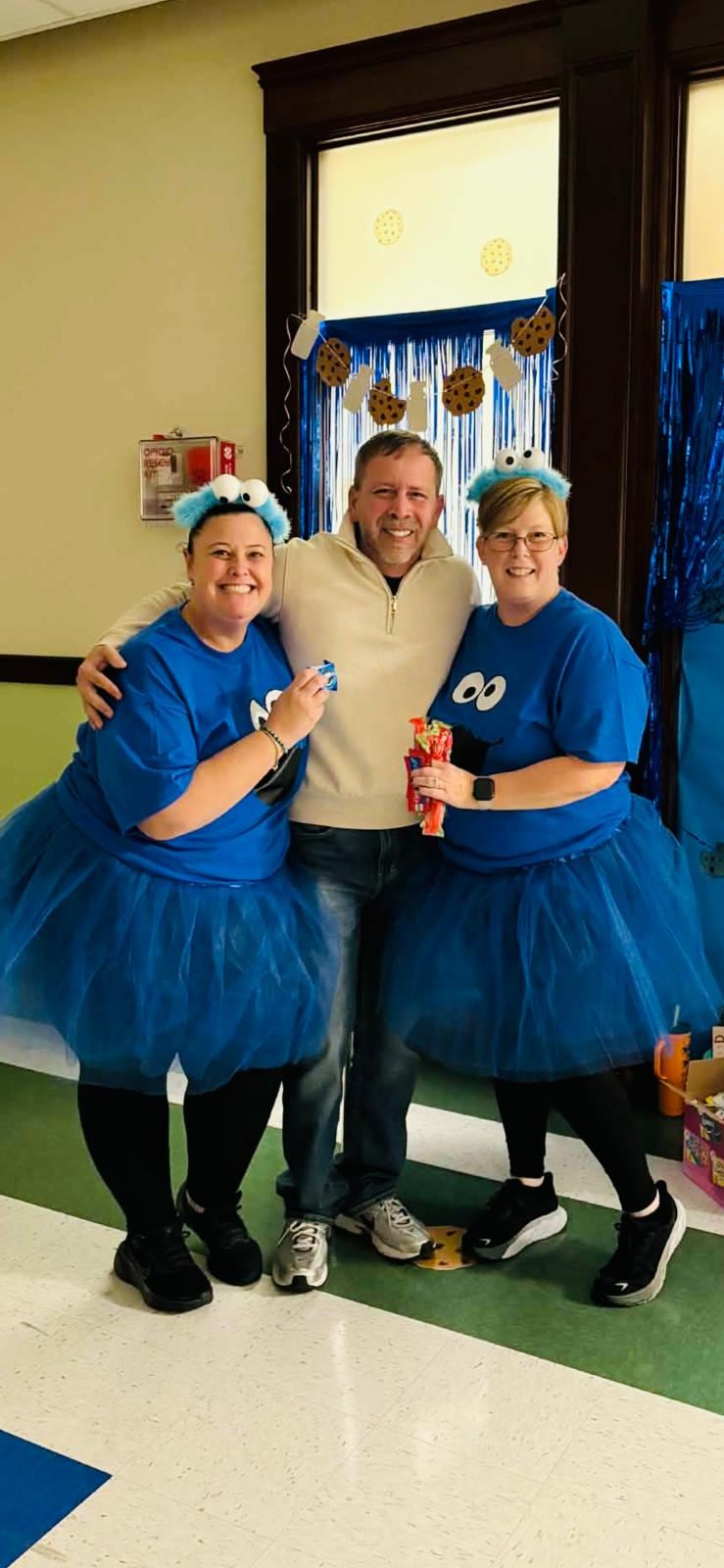 Juan Pablo Barrera poses between two women in blue character shirts, tutus, and fuzzy eye headbands.