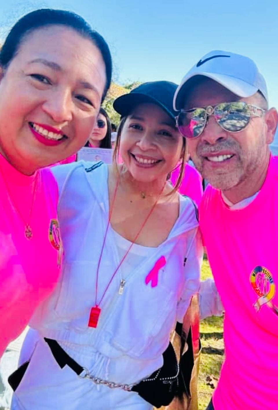 Three adults in pink tops smile for a close outdoor selfie.