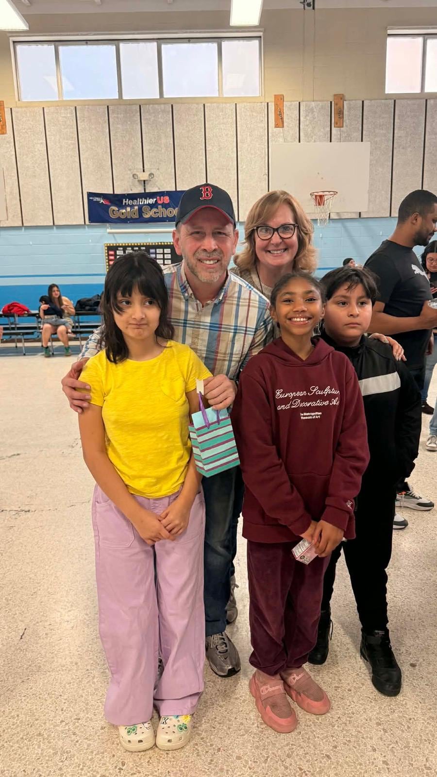Juan Pablo Barrera and a woman pose behind three children in a gym, one child holding a small gift bag.