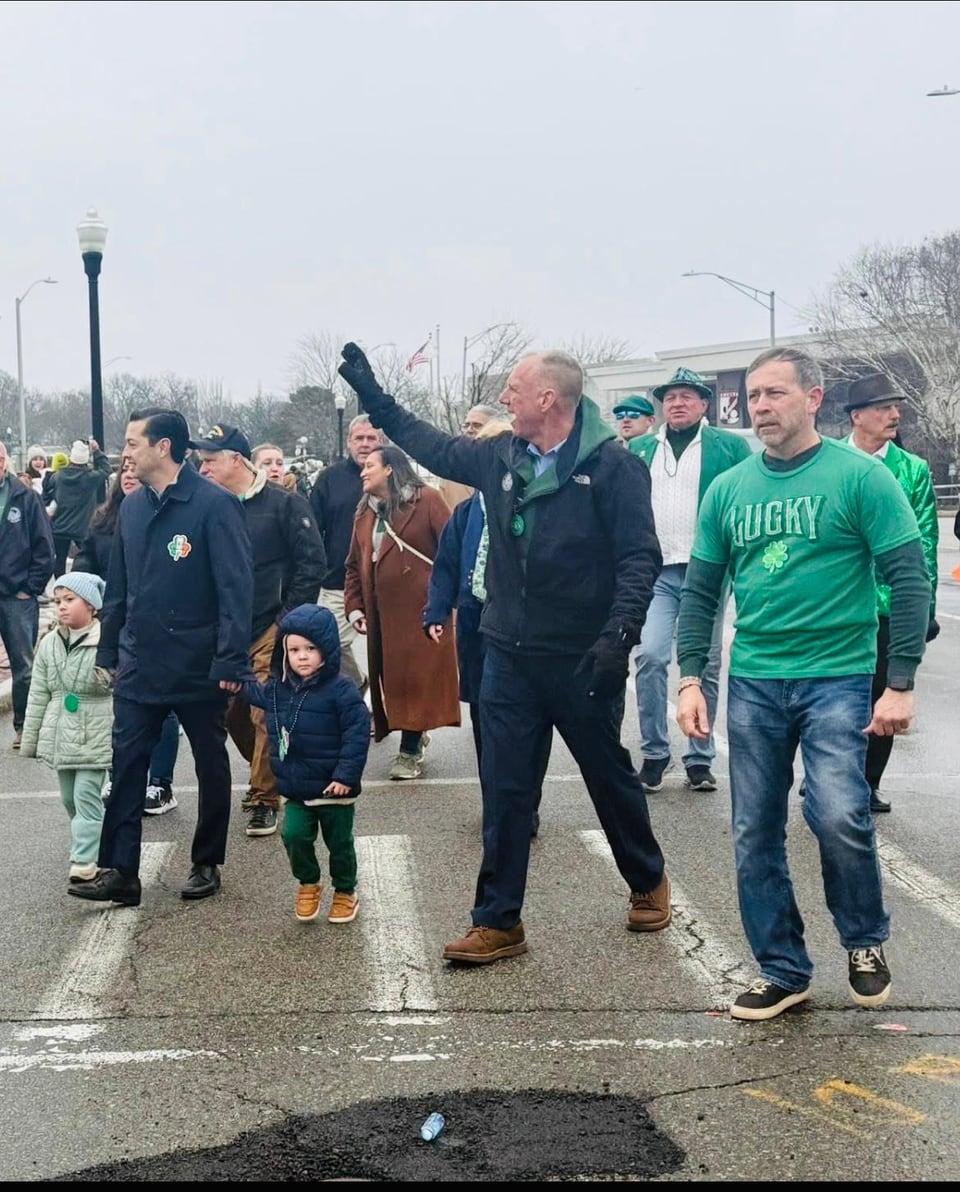 Juan Pablo Barrera in a green 'Lucky' shirt walks among adults and children on a wet street.