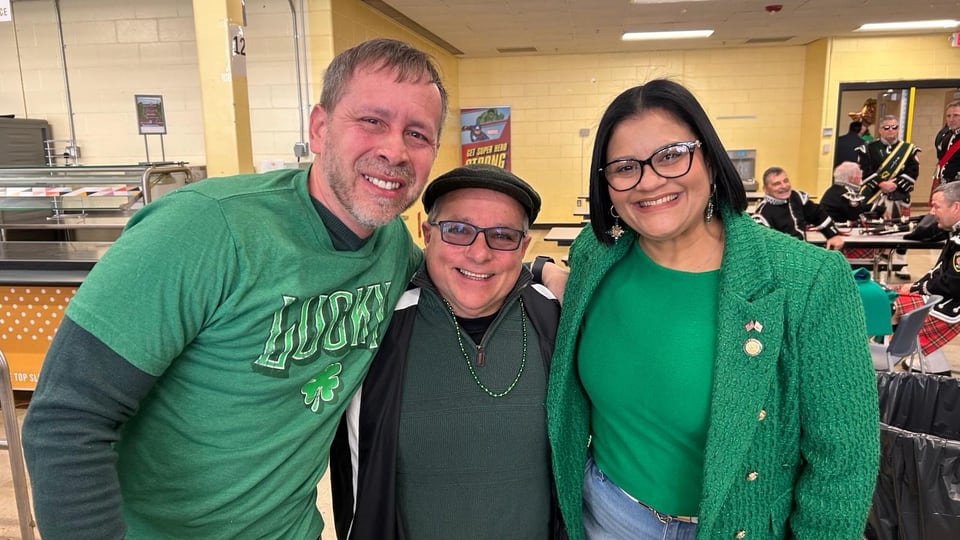 Juan Pablo Barrera and two adults in green pose closely together indoors.