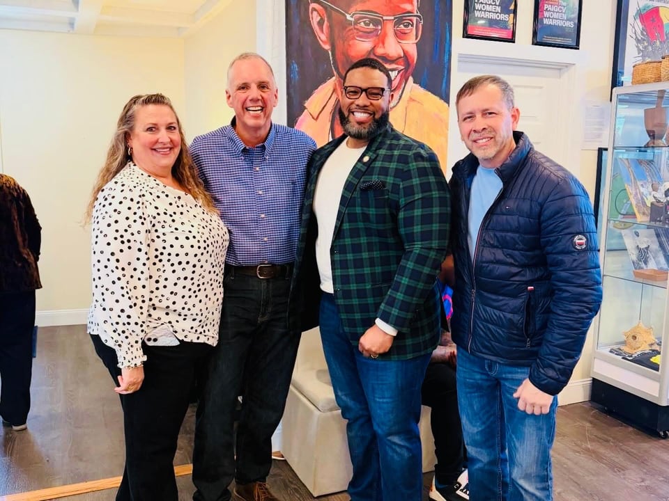 Four adults pose shoulder to shoulder in front of a colorful art display.