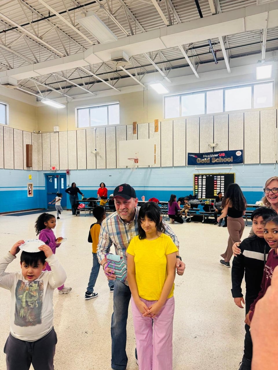 Juan Pablo Barrera bends toward two children while adults and children dance around them in a gym.