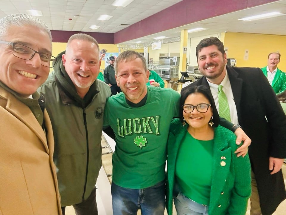 Five adults crowd together for an indoor selfie, with Juan Pablo Barrera in a green shirt at center.