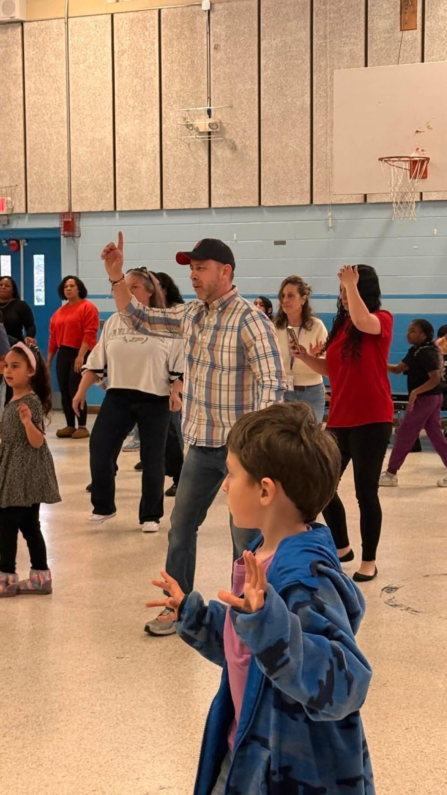 Juan Pablo Barrera raises both hands while dancing in a gym as a child watches in the foreground.