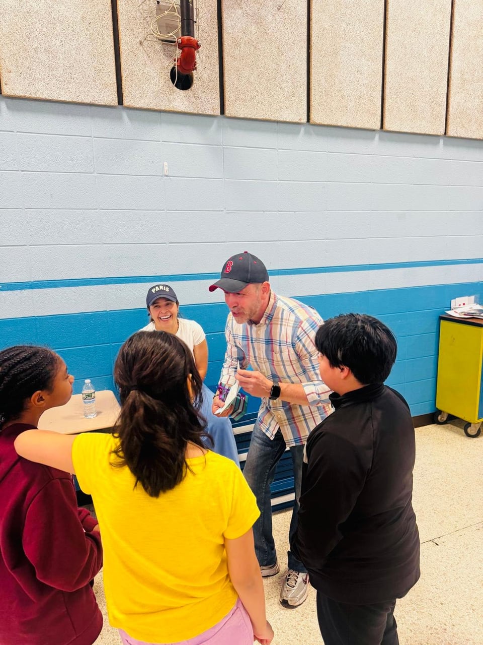 Juan Pablo Barrera leans toward children seated around a table in a gym.