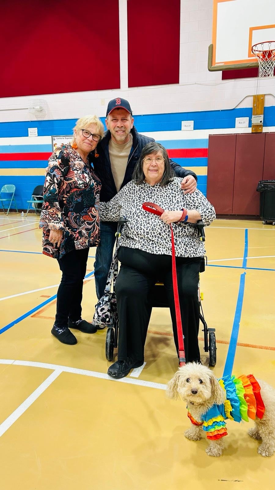 Juan Pablo Barrera poses with two women in a gym; one uses a wheelchair and holds a small dog's red leash.