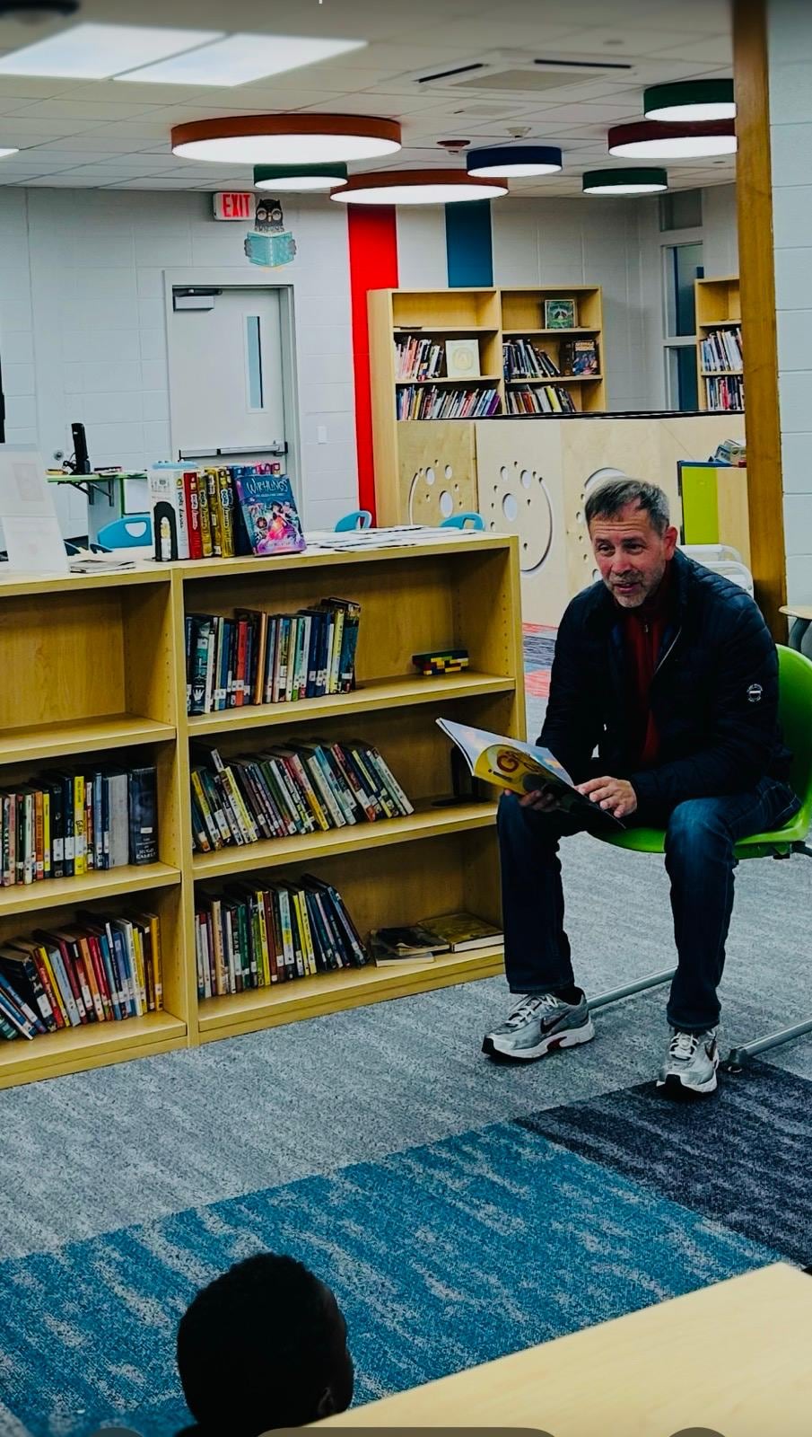 Juan Pablo Barrera sits beside low bookshelves in a colorful reading area.