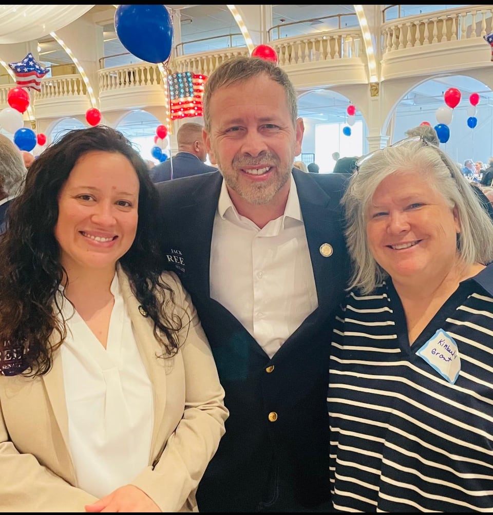 Juan Pablo Barrera smiles between two women beneath red, white, and blue hanging decorations.