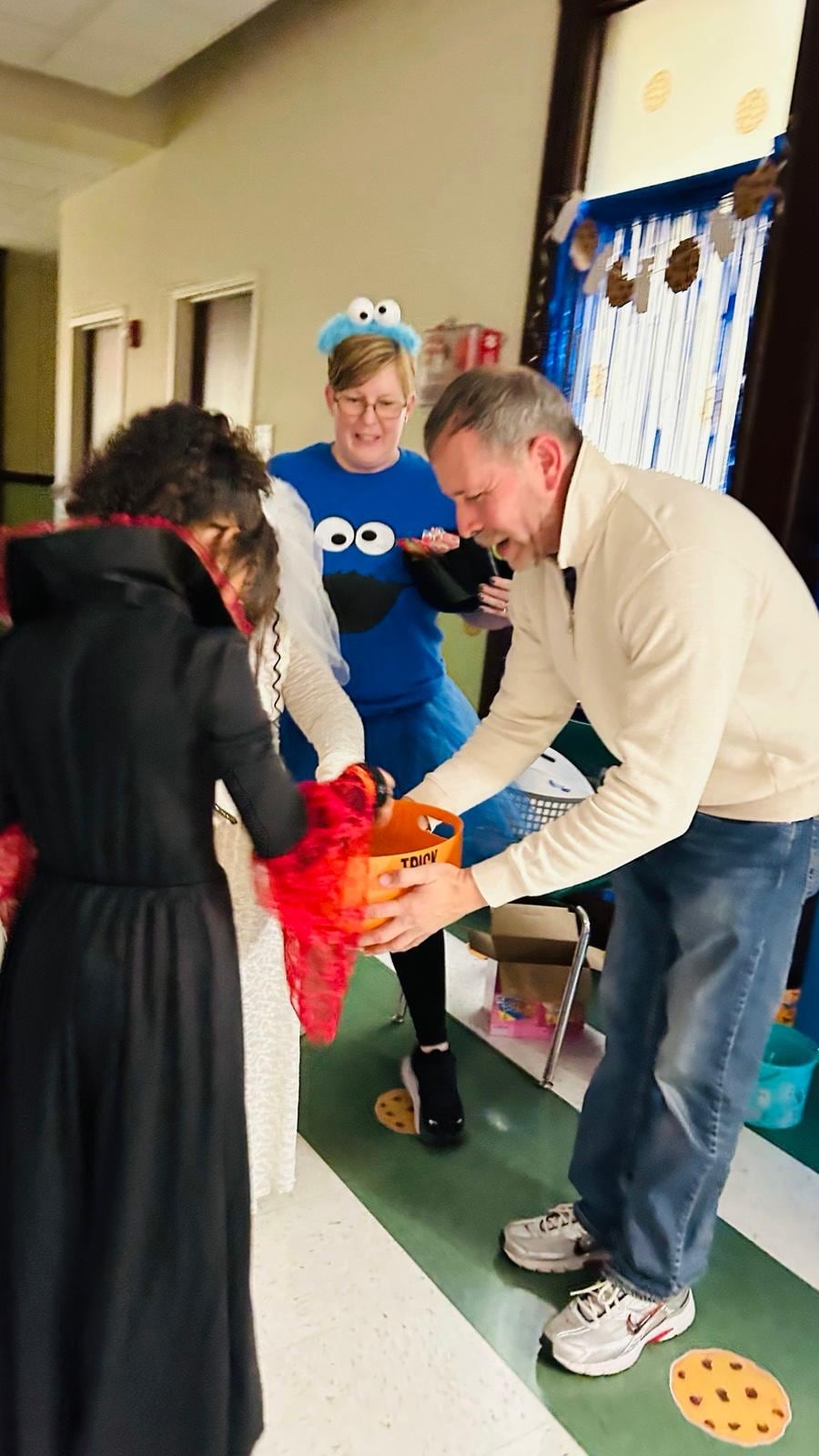 Several people gather around a table as a man bends forward holding a bright orange item.