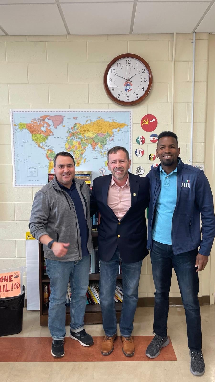 Juan Pablo Barrera poses with two men in front of a wall map and clock.