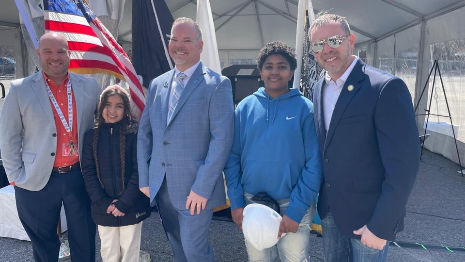 Five people stand together outdoors near an American flag, with Juan Pablo Barrera at right.
