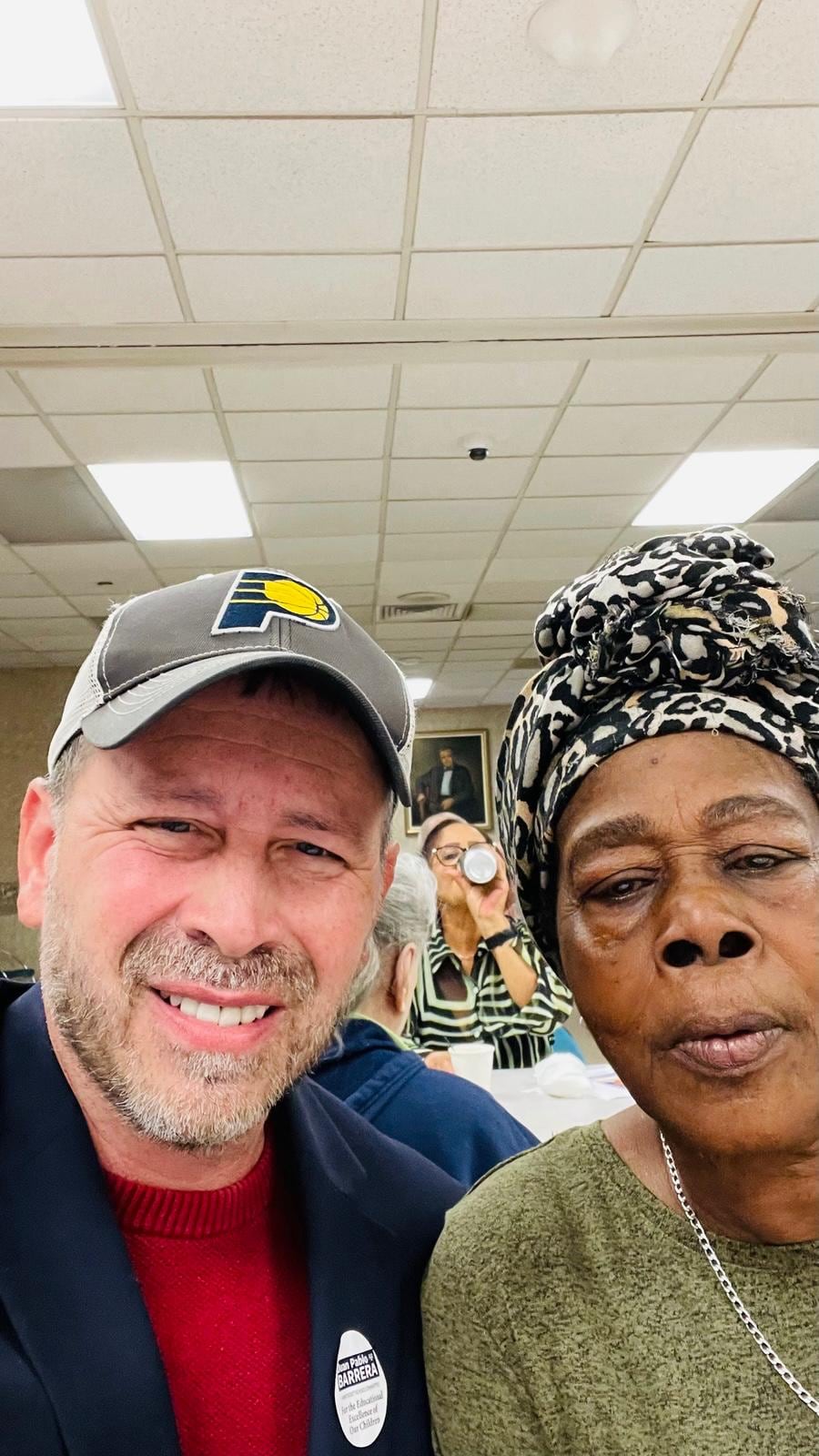 Juan Pablo Barrera smiles for an indoor selfie with a woman wearing a patterned headwrap.