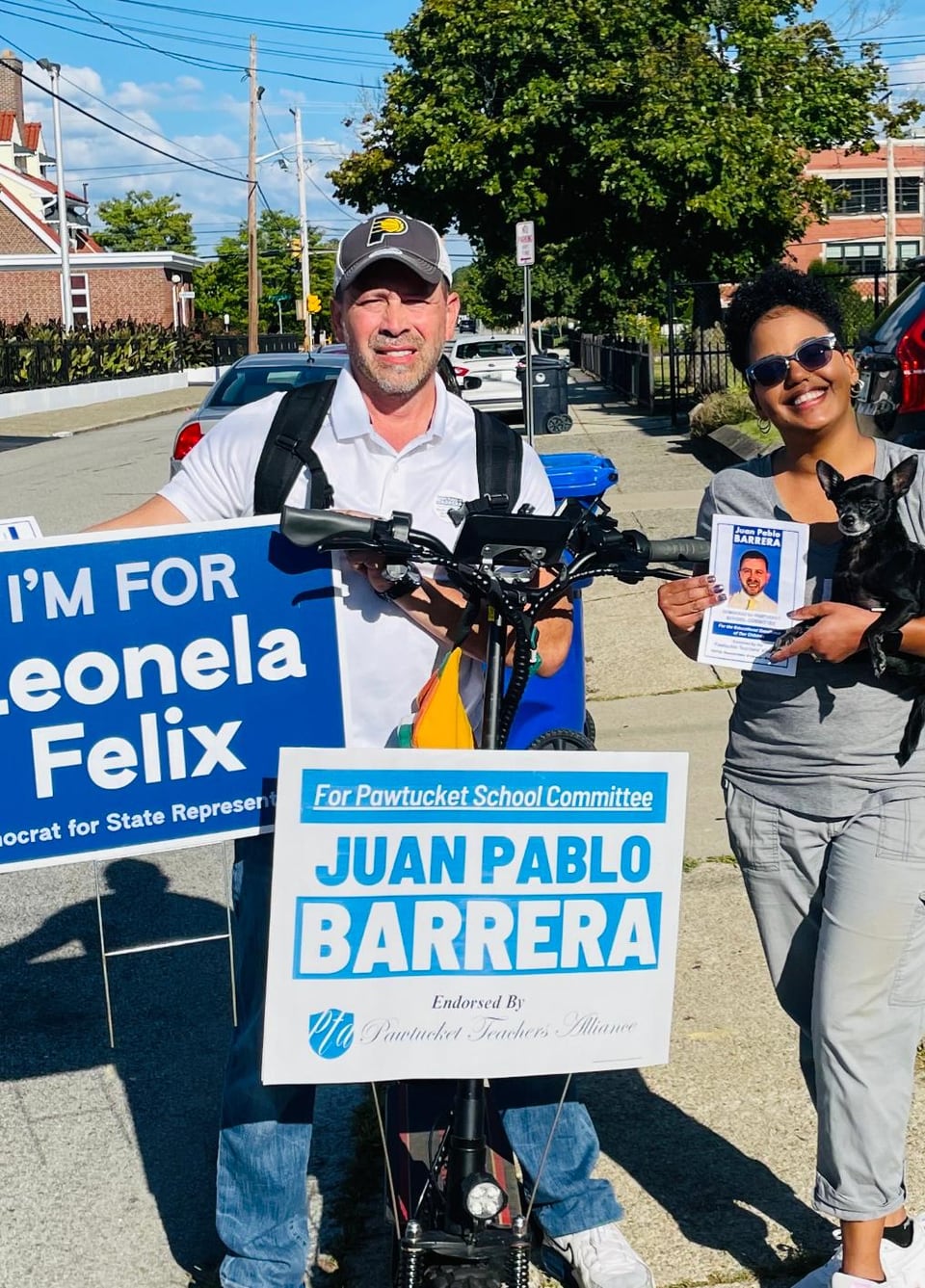 A man and woman stand beside a bicycle displaying signs with Juan Pablo Barrera's name.