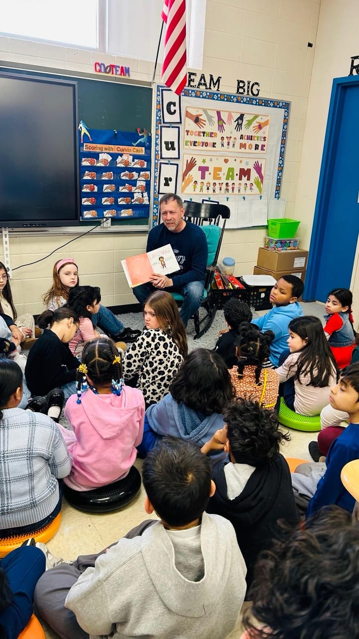 Juan Pablo Barrera seated with an open book in a classroom circle.