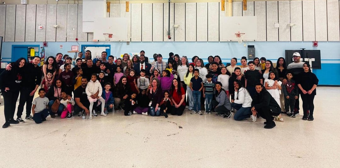 Large group of adults and children posing inside a gymnasium.
